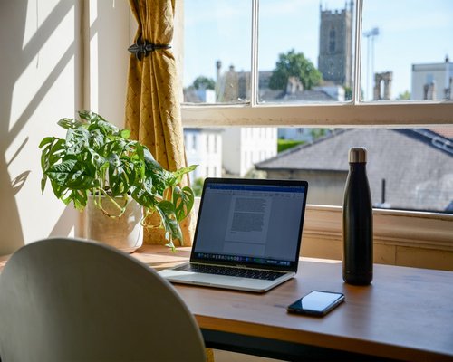 A clean and well organized home office desk featuring a laptop and natural light